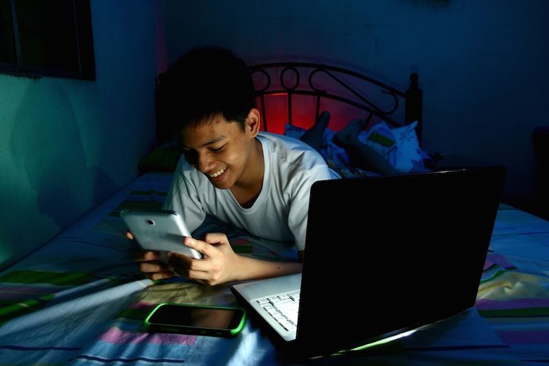 Teenager playing with electronics on bed