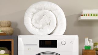 Bundled up white comforter sat on top of a white front load washing machine.