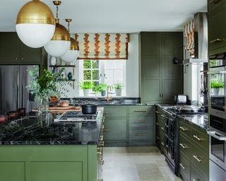 kitchen with green cabinets and island, black worksurface, brass globe lights and patterned blinds