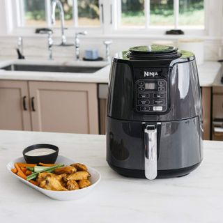 A black Ninja air fryer with cooked chicken wings on plate, served alongside carrot and celery crudites with creamy dip
