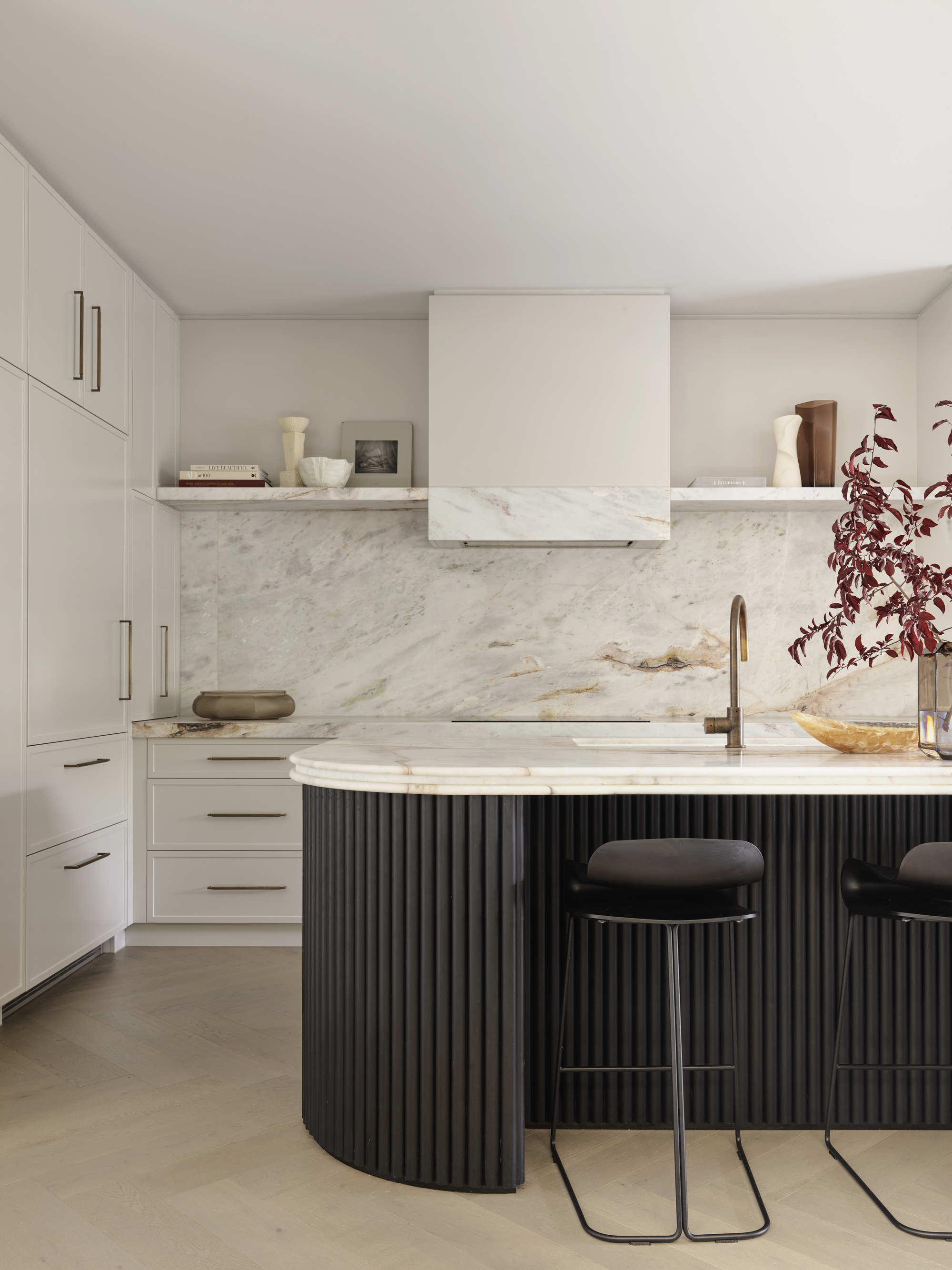 Image of a white kitchen with marble countertops and backsplash. The island is black with slim black barstools