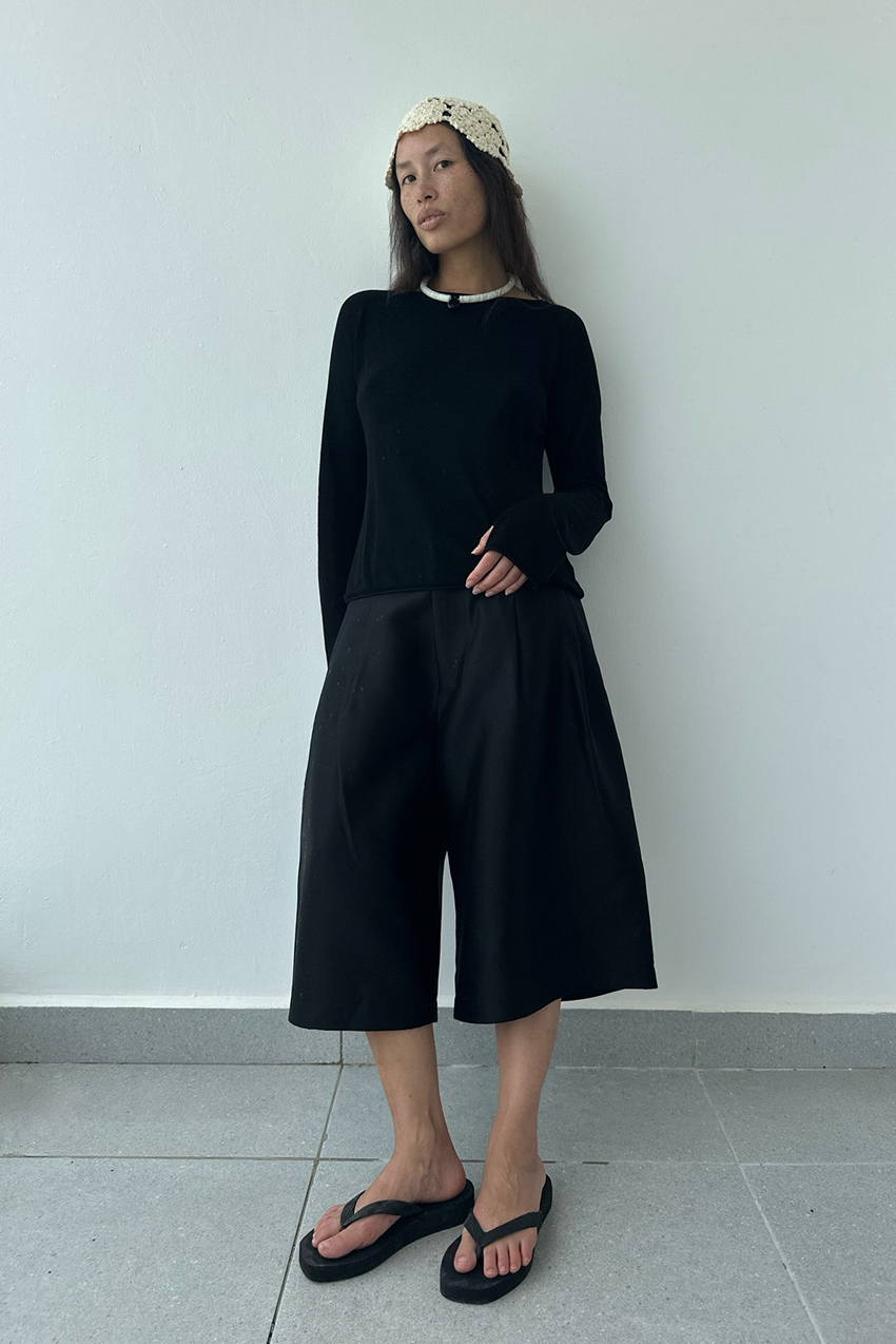 a woman wearing a black longsleeve, black silk shorts, and black flip flops