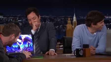Jimmy Fallon laughing at laptop on desk.