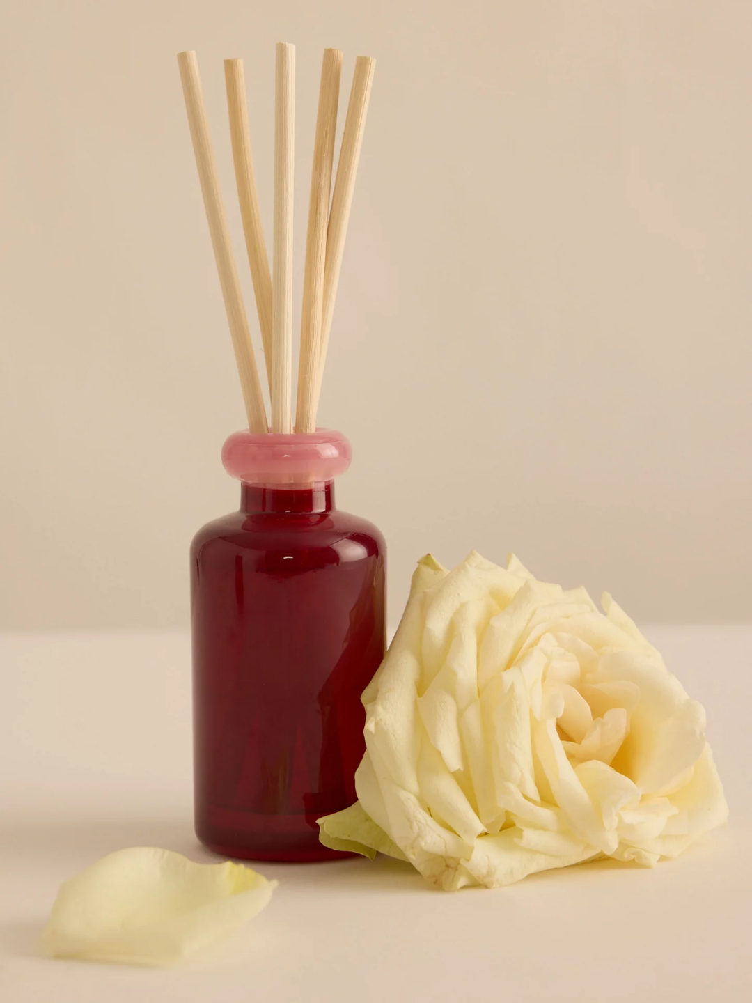 A red glass reed diffuser by a white rose head