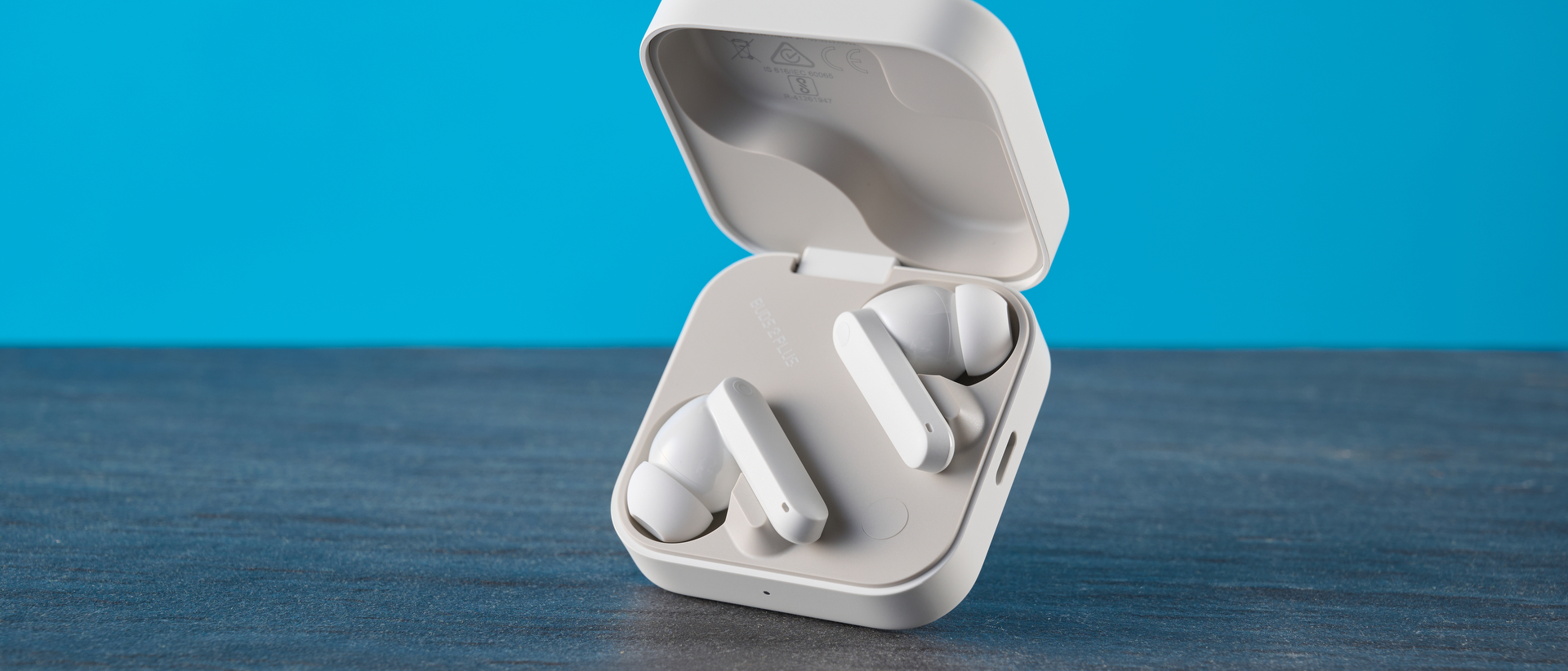 CMF Buds 2 Plus in light gray photographed in front of a blue background