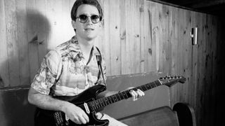 Marshall Crenshaw, holding his guitar, as he sits on a banquette backstage at the nightclub My Father's Place, Roslyn, New York, June 26, 1982.