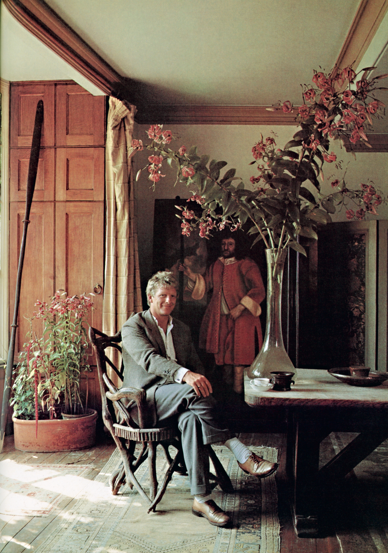Christopher Gibbs, sitting in a wooden chair at some point in the 1980s or 90s.