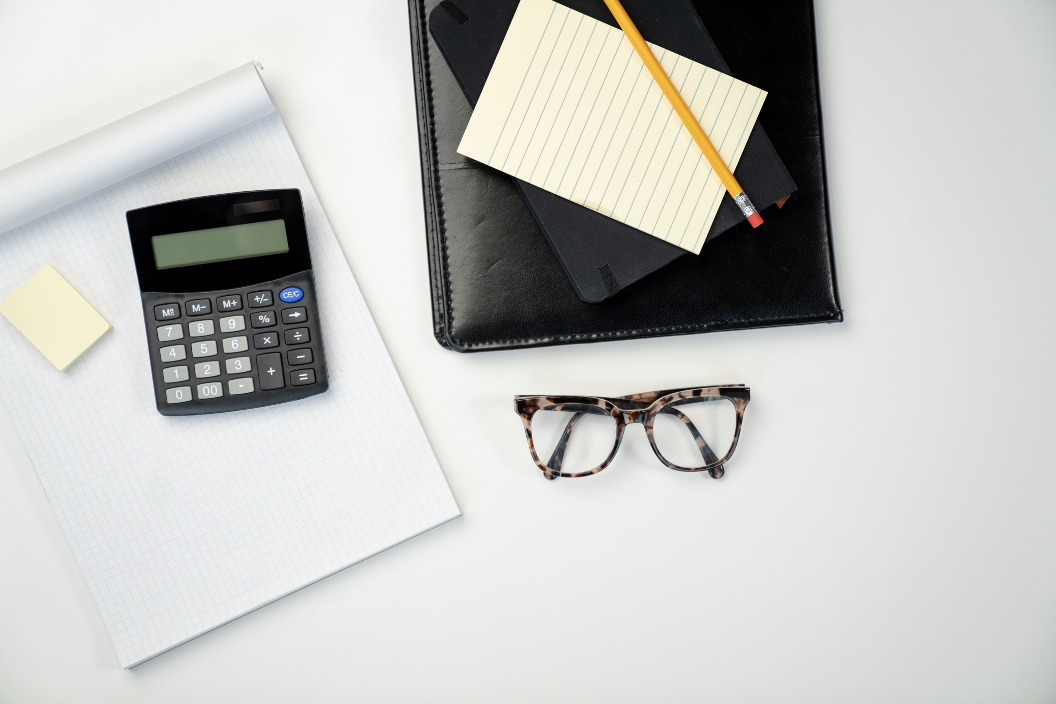 glasses, calculator, pencil and paper on a white desk