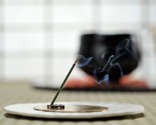 An incense stick burning on a flat circular gold and white holder with a blurred background