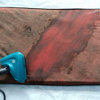 Closeup of a Hoover steam cleaner brush head removing dirt from a red outdoor cushion