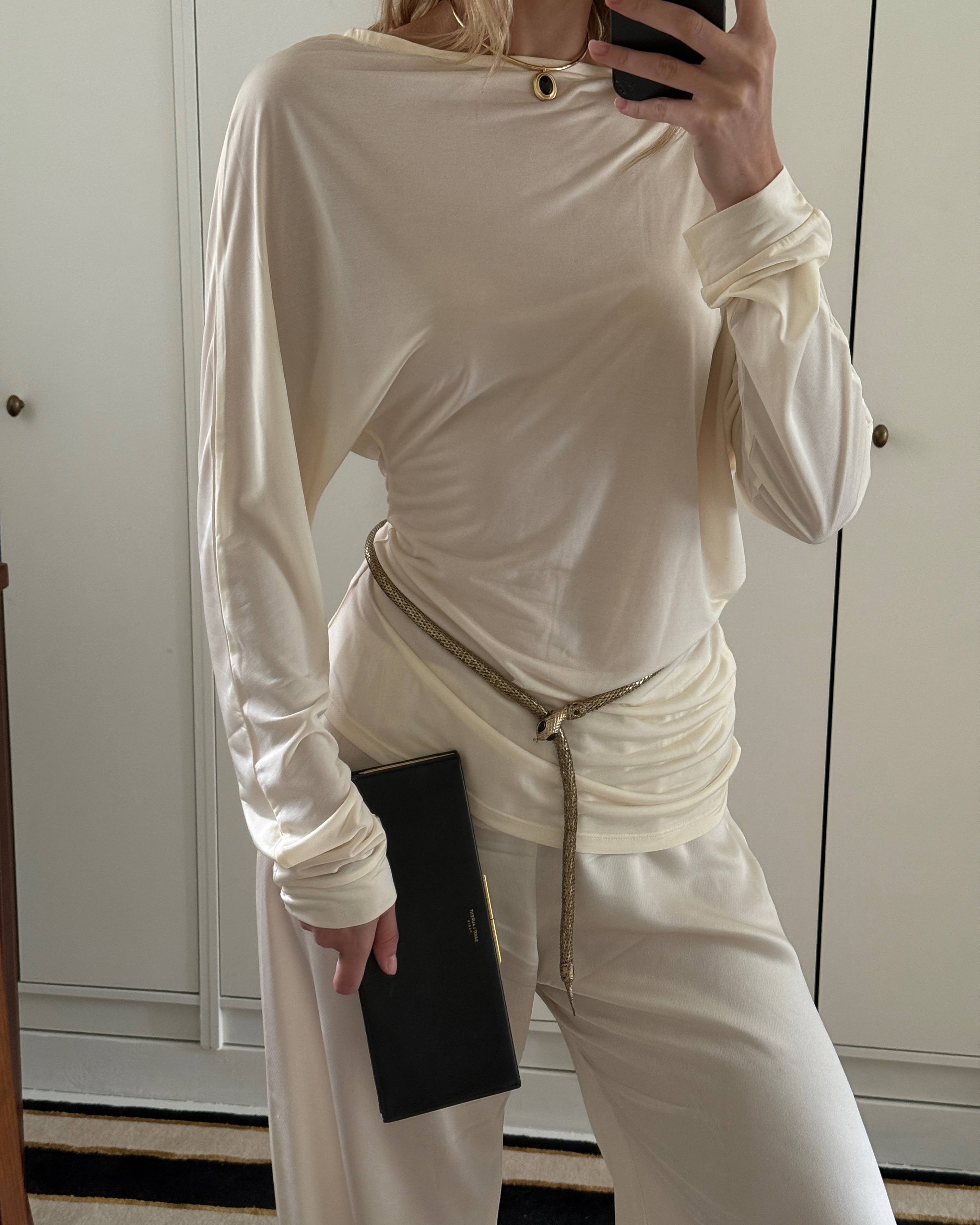 Christie Tyler wearing a white sweater with a belt and a clutch.