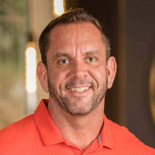 Image of a man with a beard in a bright orange collared shirt.