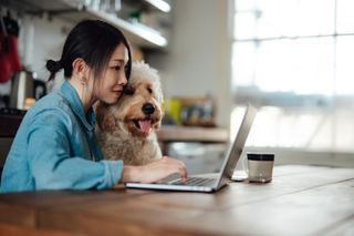 A woman and her dog sit at a table in front of a laptop