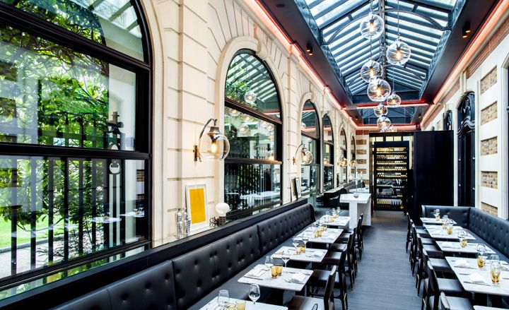 Italian cafe with glass roof and large windows and geometric patterns on walls and lined with charcoal leather banquettes