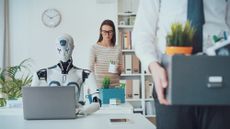 A robot sits at a desk while people back their belongings in boxes