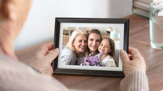 Dragon Touch Classic 10 Digital Picture Frame displaying a family while held in someone's hands