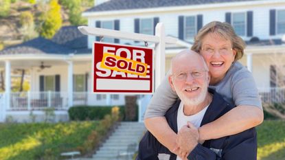 elderly couple next to sold sign in front of a home