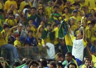 Kaka holds aloft the World Cup in 2002 as Brazilian fans celebrate in the background.