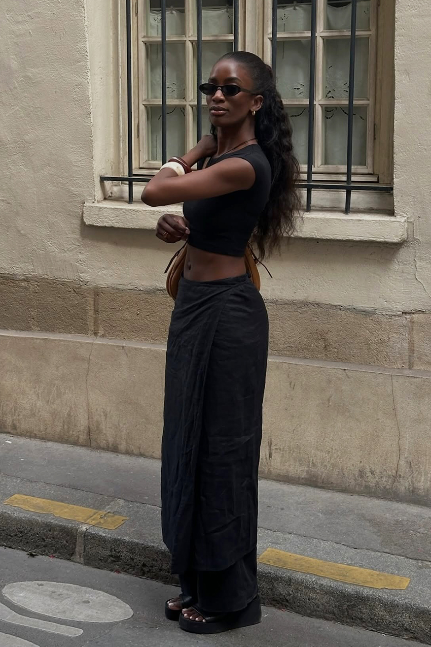 A woman wearing a black tee, black pants, and black wedge sandals.