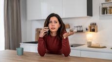 A woman looks frustrated on the phone while sitting at her kitchen island.