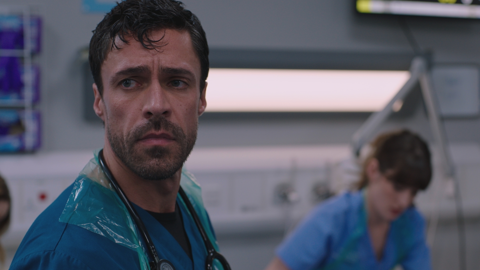 Clinical lead Flynn Byron looking stressed and worried while Jodie treats a patient in the background.