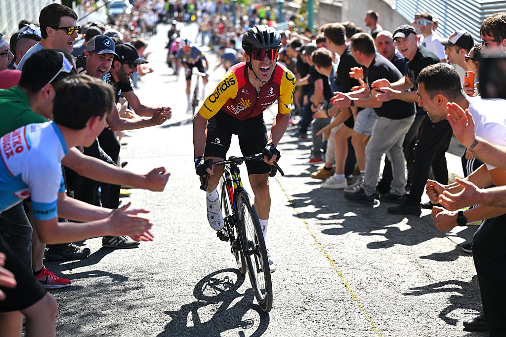 Izagirre out of the saddle grimacing as Basque fans surge into the road cheering him on, Simmons is in the distance behind
