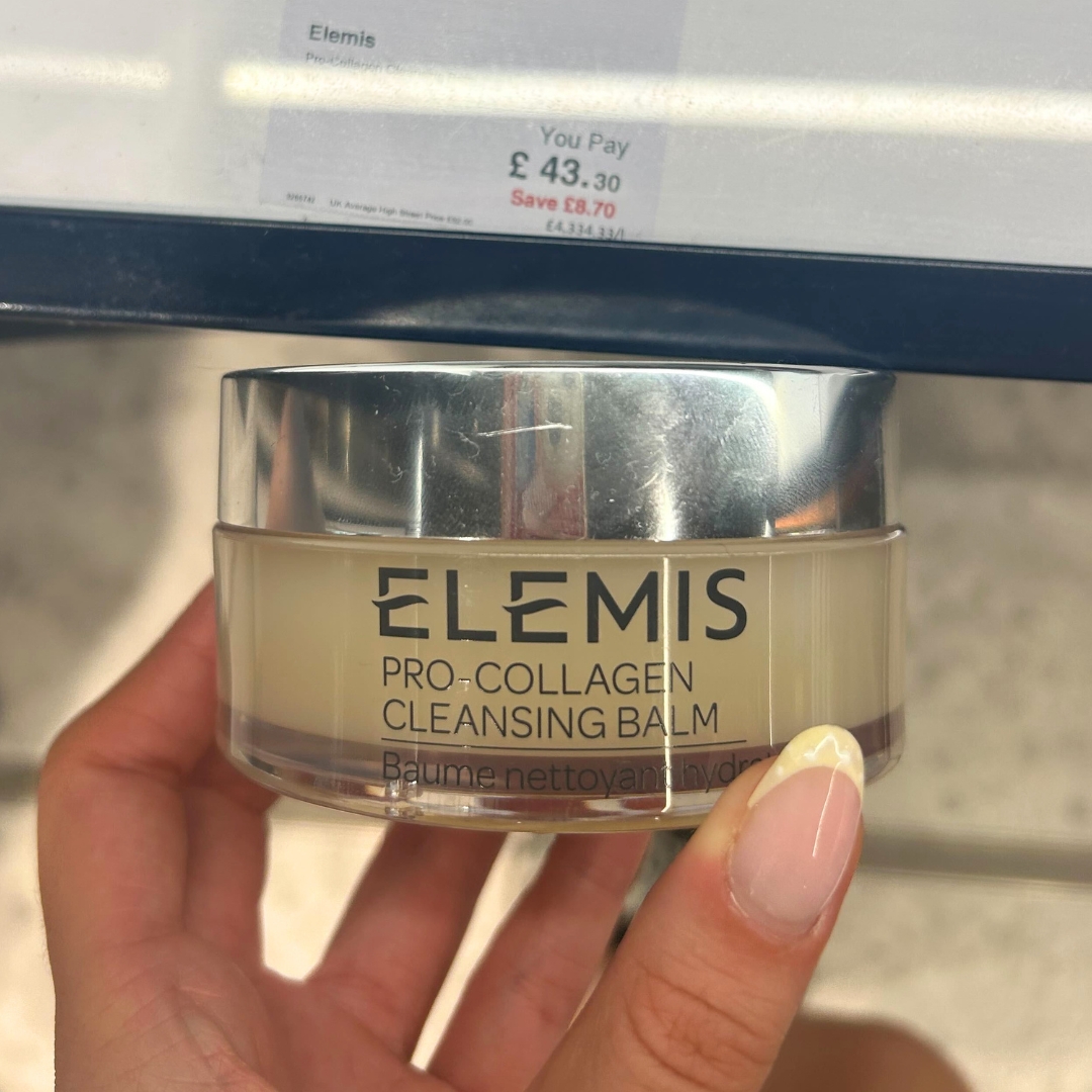 Hand holding tub of Elemis Pro-Collagen Cleansing Balm in World Duty Free
