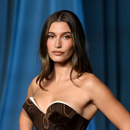 a woman with dark hair posing for paparazzi in a brown strapless gown at a red carpet event