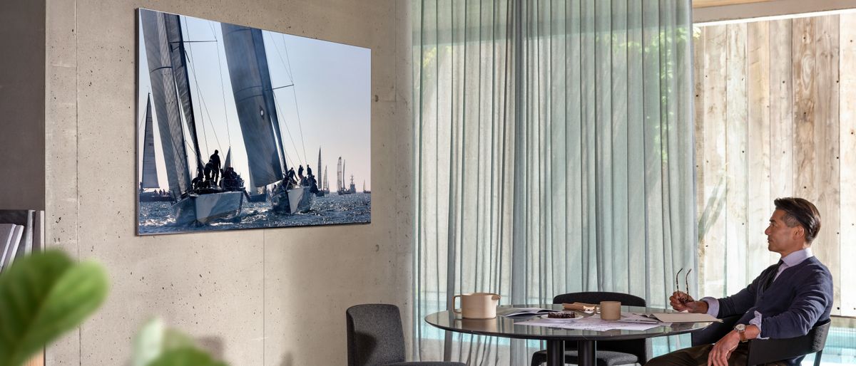 Samsung Q950TS 8K QLED TV hanging on wall while man watches over table