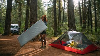 A camper inflates her Therm-a-Rest sleeping pad next to her tent