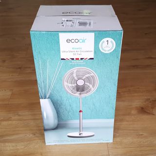 The EcoAir Kinetic fan in its blue and white packaging box on a wooden floor