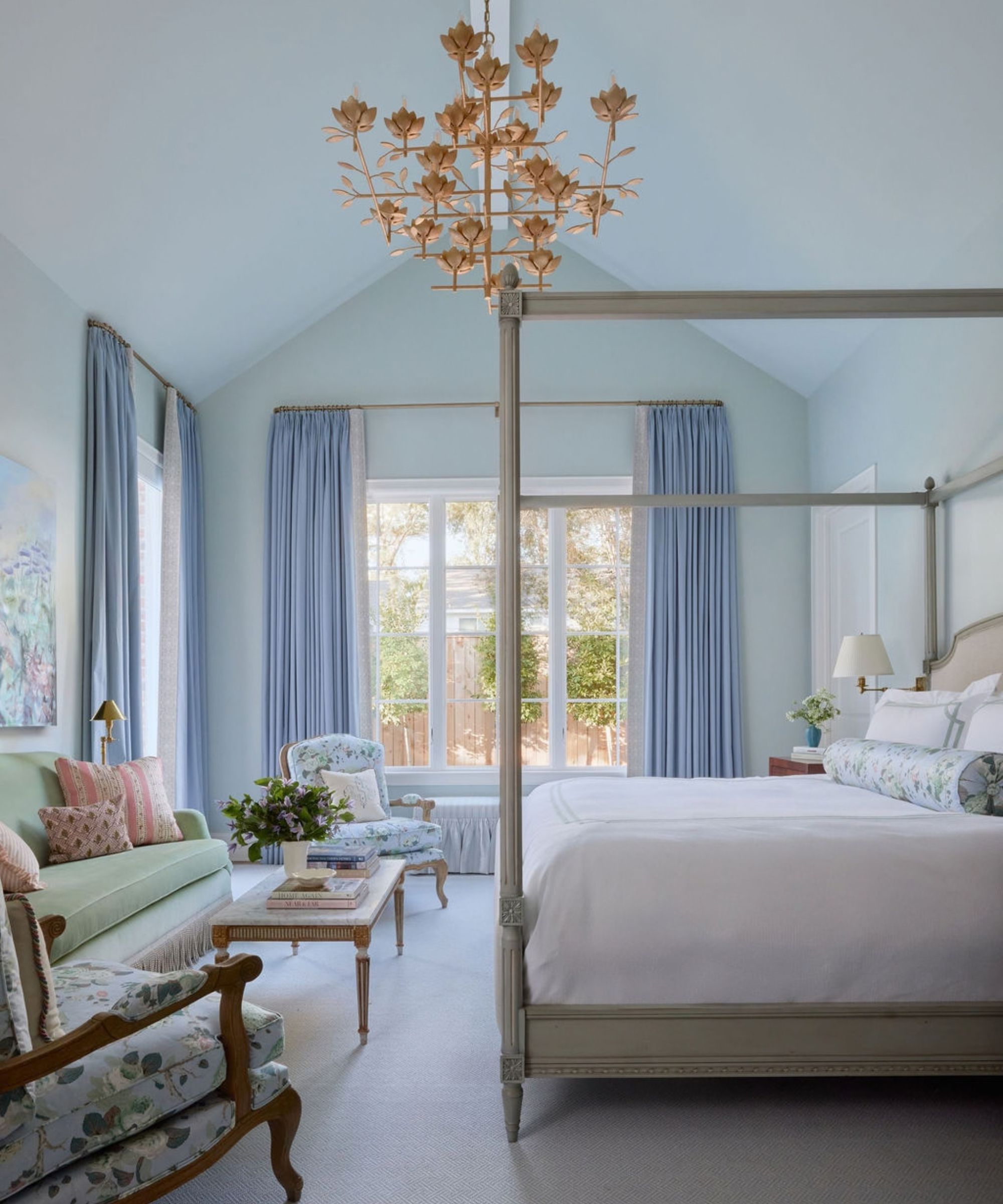 Light blue bedroom featuring a four-poster canopy bed, vaulted ceiling, floral accents, and a gold leaf chandelier