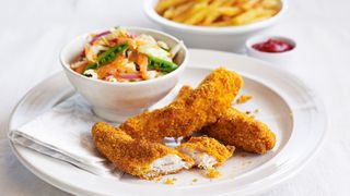 Dinner plate with breaded chicken pieces which you can cook in an air fryer, served with a slaw salad and chips