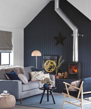 living room with midnight blue feature wall, white ceiling and walls, grey floor, blue rug and furniture, wood burning stove, and colourful decorative touches
