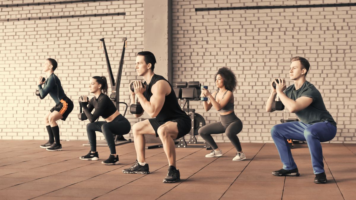 Group of people performing goblet squat with dumbbells in gym