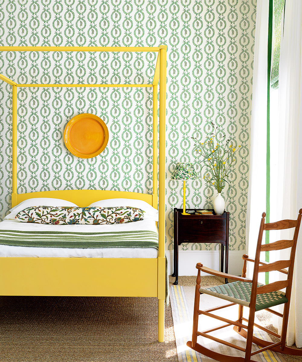 Colourful bedroom ideas showing a bright yellow four poster bed and patterned green wallpaper