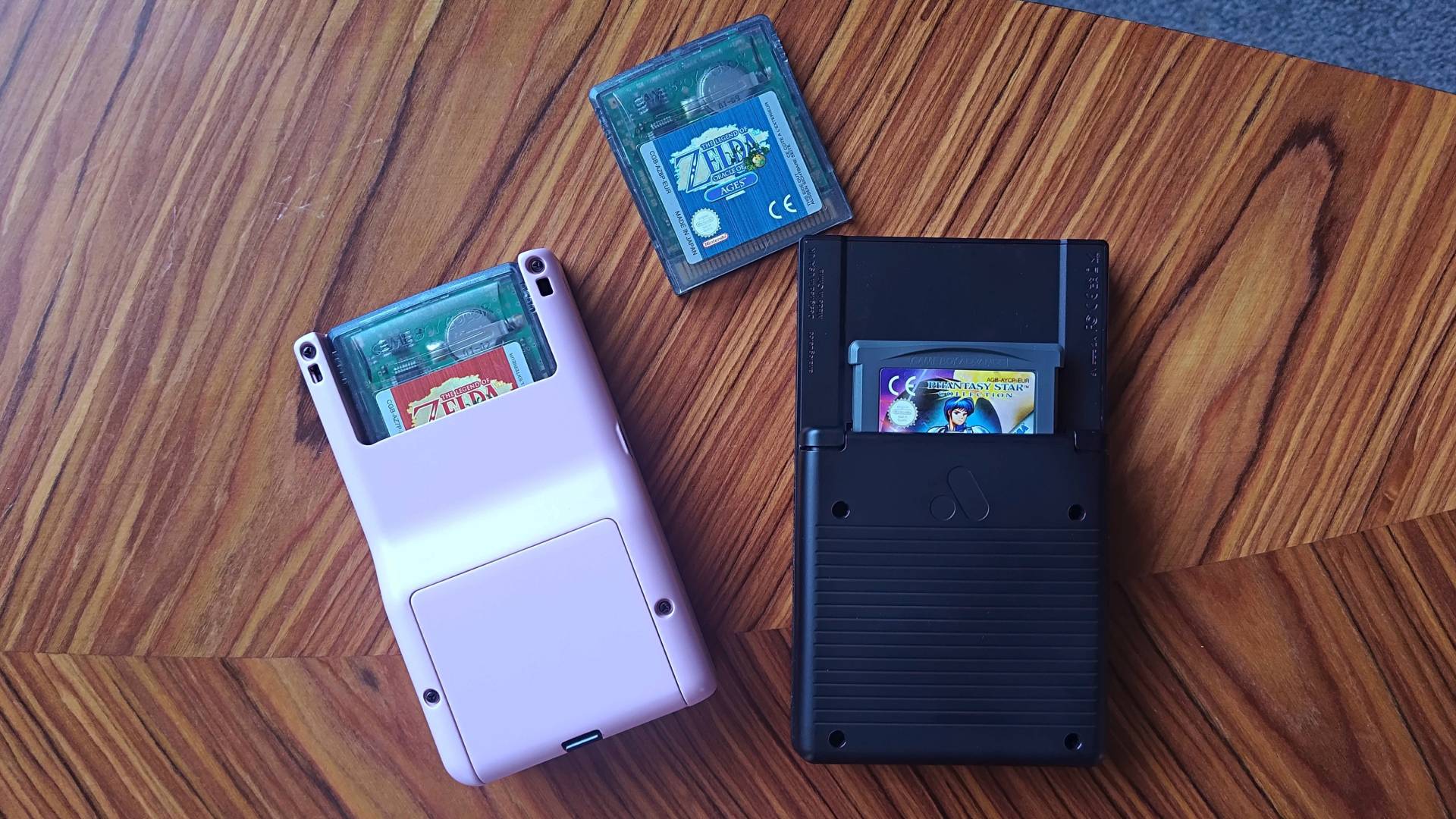 Back view of Modretro Chromatic and Analogue Pocket handhelds with Zelda: Oracle of Seasons inserted into Chromatic and Phantasy Star Collection GBA into Pocket with Zelda: Oracle of Ages in middle.