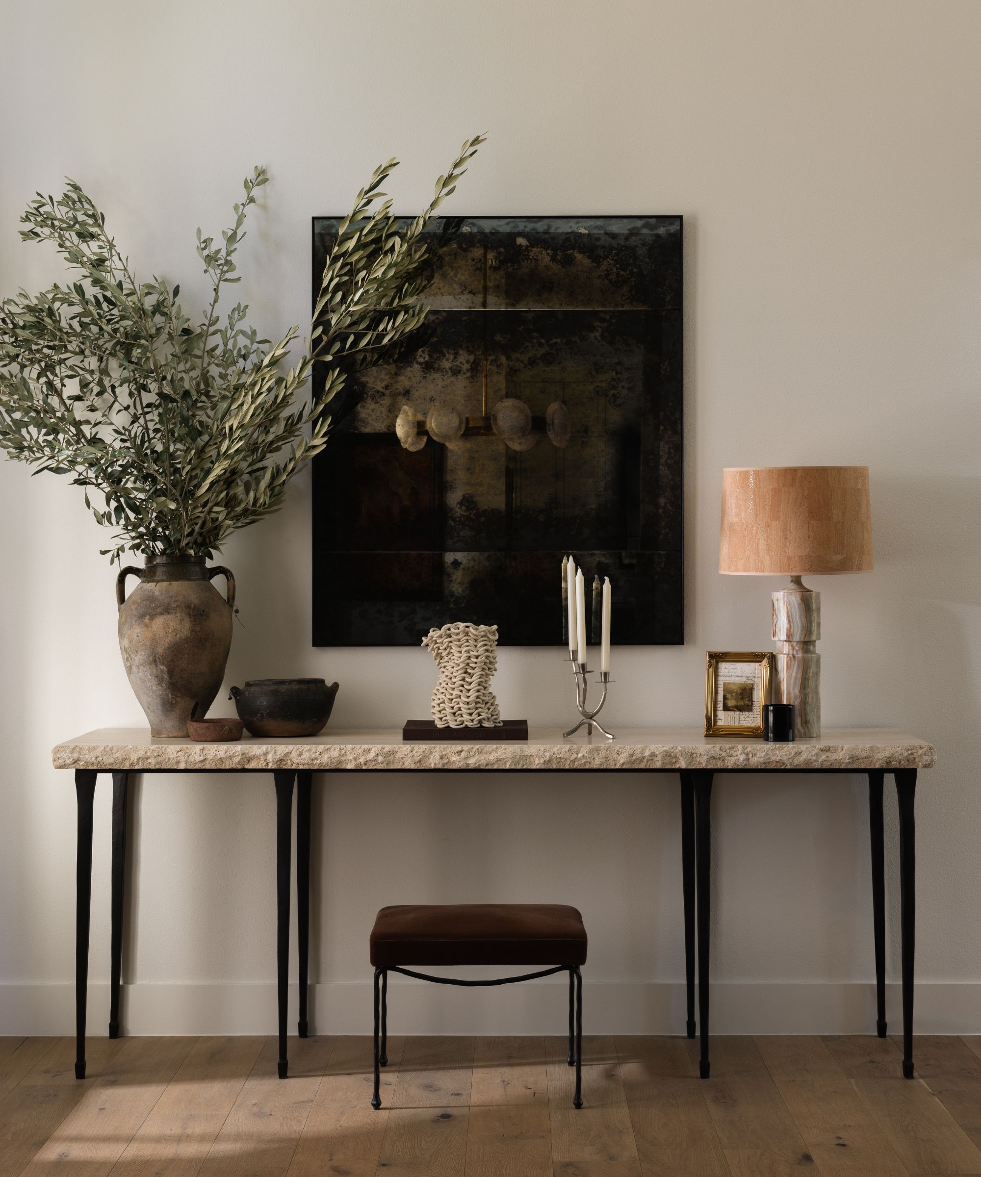 a neutral entryway with a stone and metal table, large vintage mirror and styled with a rustic vase, table lamp and small objects