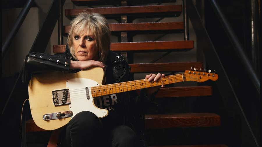 Lucinda Williams sitting on some stairs holding a guitar