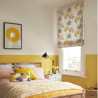 a yellow painted bedroom with double bed and patterned roman blind hung over the window