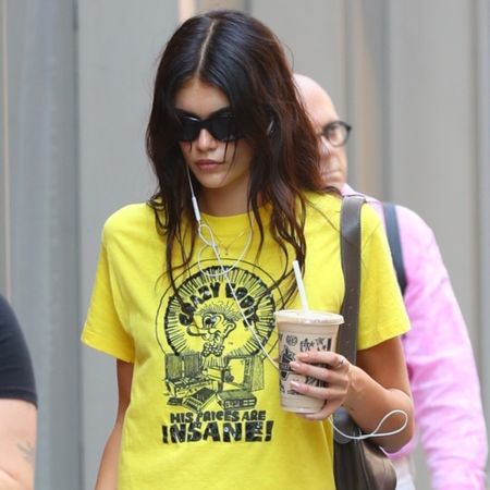 Kaia Gerber wearing a yellow graphic T-shirt with a white midi skirt and ballet flats in NYC.