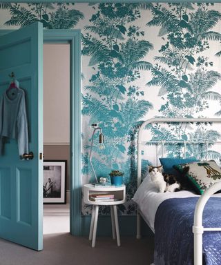Bedroom with a metal bedstead and bed, turquoise paintwork door and vibrant turquoise blue patterned wallpaper