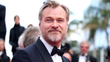 Christopher Nolan smiling in a tuxedo at the Cannes Film Festival, with his hair blowing in the wind.