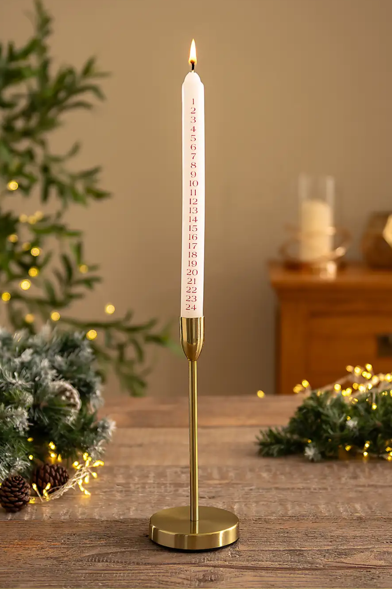 A white advent candle with red markings on a gold holder