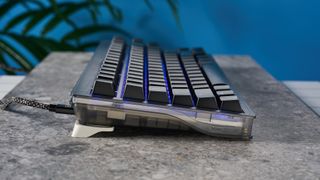 The Wooting 80HE in Ghost PCR case with black keycaps, on a stone surface with a blue background.