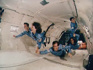 STS-51L payload specialists appear to float momentarily in a human chain inside the KC-135 aircraft during zero-g training.