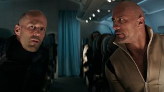 Hobbs and Shaw looking at each other while sitting on an airplane.