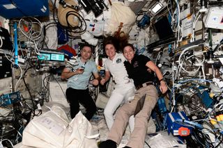 three astronauts in the middle of a module absolutely stuffed with equipment, spacesuits and electronics