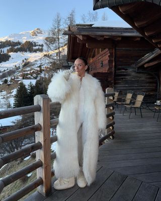 Emma wears a white fur coat, white moon boots, and a white ski suit.