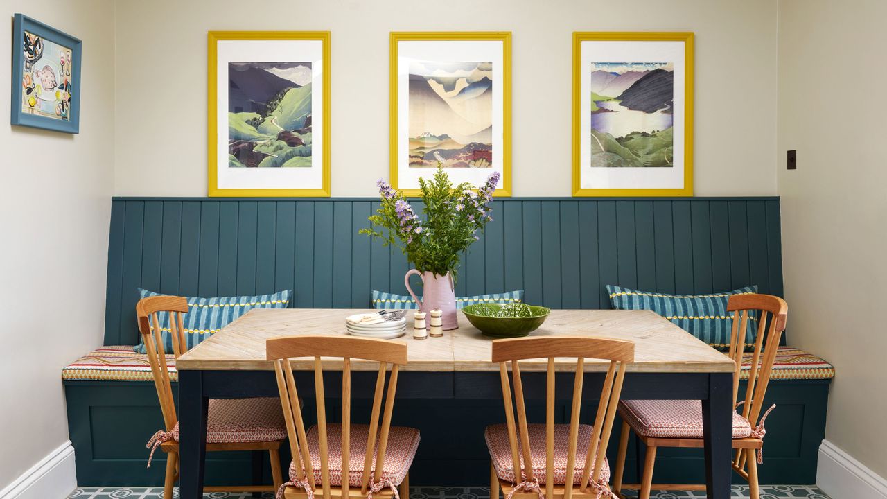 gallery wall ideas yellow framed artwork on cream wall behind dark blue panelling banquette seating area which is paired with table and farmhouse chairs